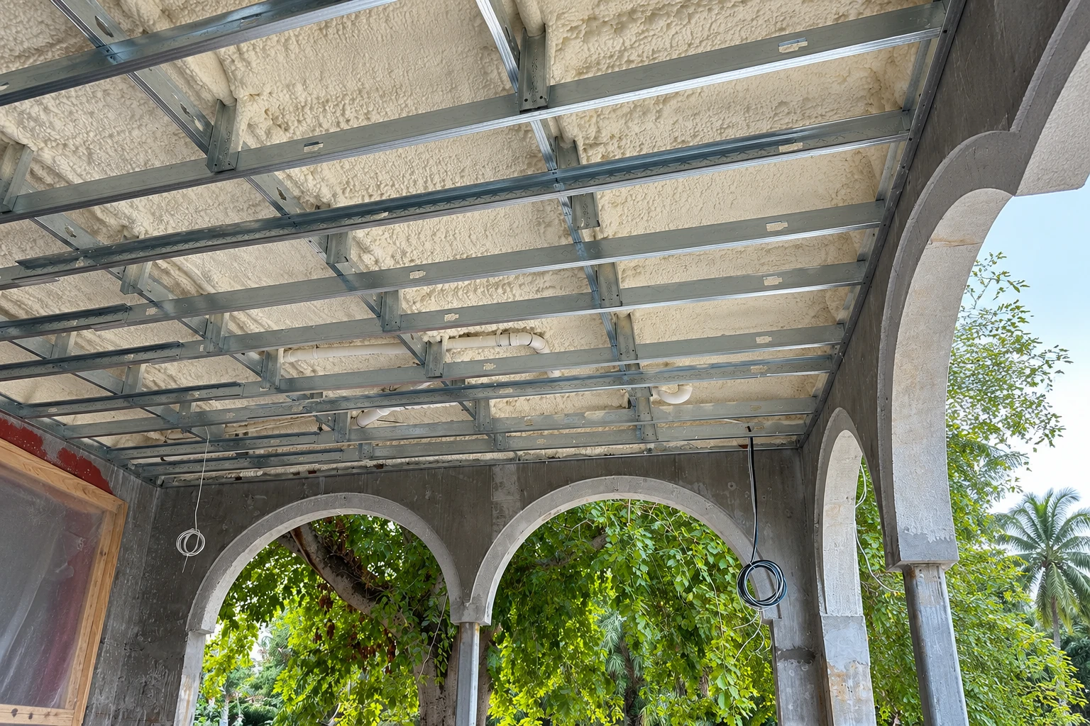 Spray foam fills the ceiling above metal framing in an open-sided structure with stone arches.