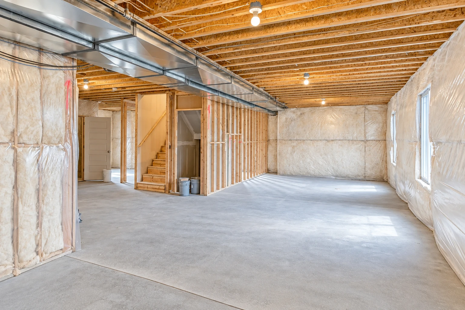 Basement with insulation covering the walls, exposed ceiling joists, metal ductwork and a concrete floor.