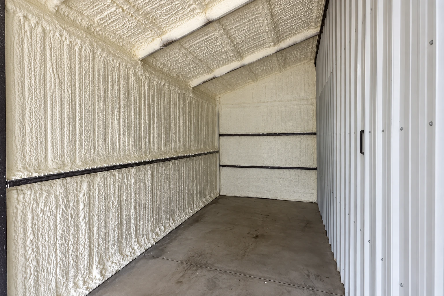 Narrow room with textured white spray foam coating the walls and sloped ceiling beside a metal panel wall.
