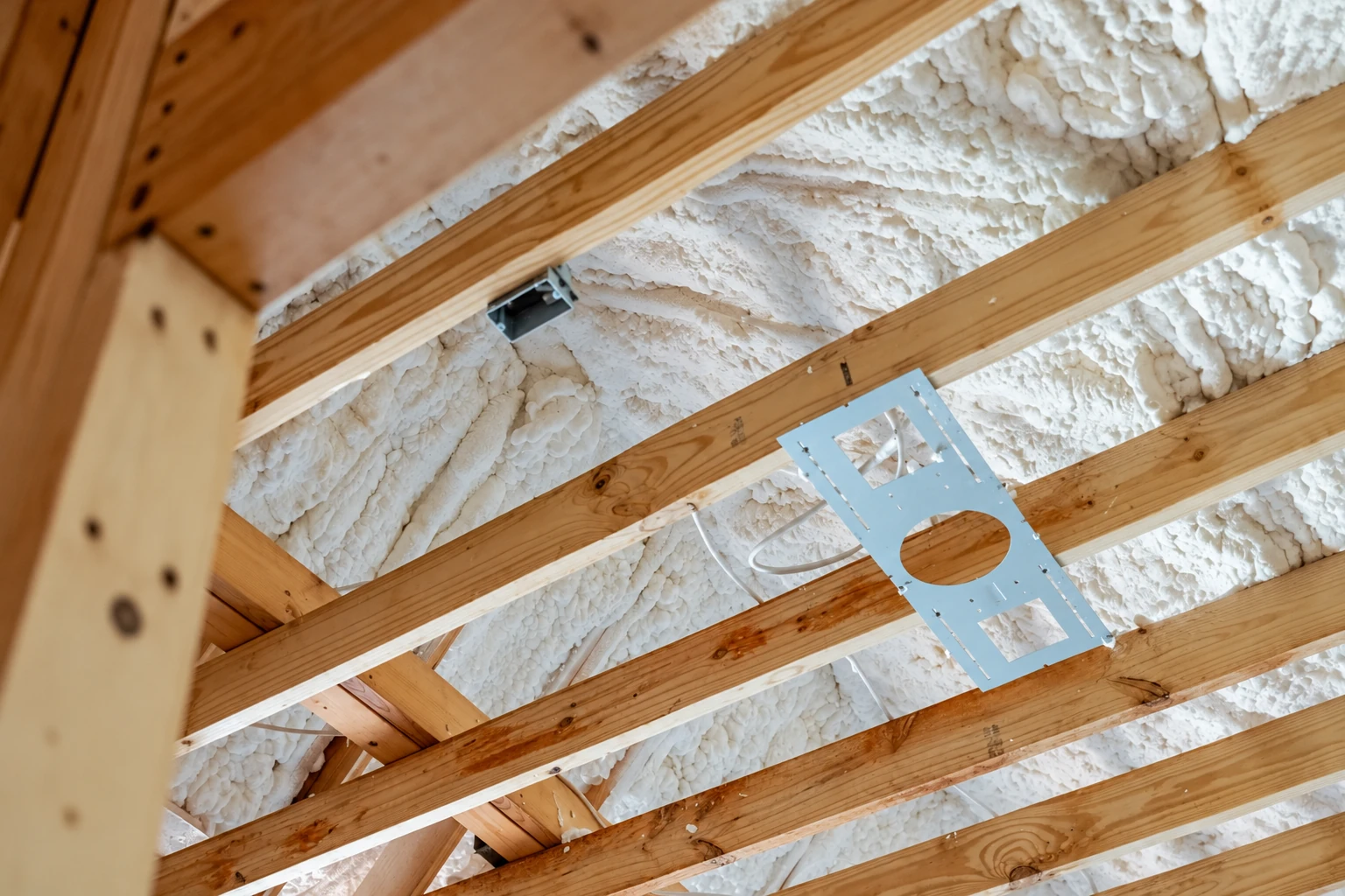 Open-cell spray foam fills the roof cavities between exposed wooden rafters.